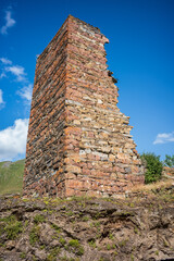 Historic stone tower ruins standing tall against a bright blue sky in the Georgian mountains. A striking view of medieval architecture, heritage, and history surrounded by nature