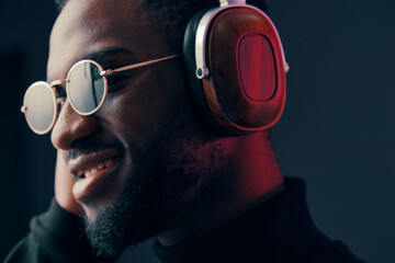 Obraz premium Stylish young man enjoying music with headphones, wearing sunglasses, showcasing a vibrant and modern look with a joyful expression in a dark background