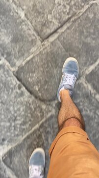 Male tourist walking on stone road or sidewalk in European old town during summer. Exploring city and sightseeing by foot. Top down point of view shot of feet and shoes. Visiting old sites in vacation