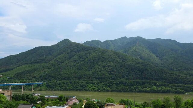 Sweeping aerial pan reveals the New Cheongpyeong Bridge crossing the Bukhan River after showcasing the lush green Cheongpyeong Valley mountains in Gapyeong