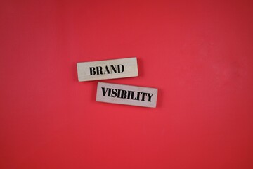 Wooden blocks with the words Brand and Visibility against a red surface, symbolizing marketing and advertising concepts.