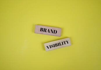 Wooden blocks with the words Brand and Visibility against a yellow surface, symbolizing marketing...