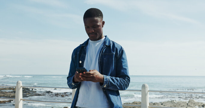Scroll, message and man at promenade with phone, communication or typing on mobile app. Concentration, digital and African male at beach with tech, connection and text update on social media.