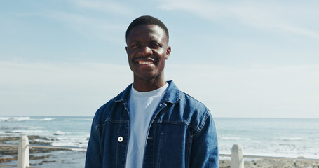 Happy, portrait and black man at beach for travel, sightseeing and weekend getaway in summer. Confident, smile and person outdoor on promenade with space, vacation and holiday break for wellness.