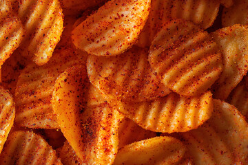 Close-up of spicy ridged potato chips covered with chili seasoning, crispy texture and golden color, snack food background
