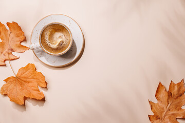 Cup of coffee on beige background with autumn yellow leaves and copy space, seasonal backdrop