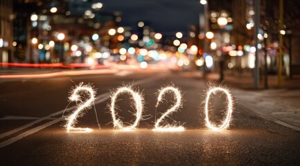 Bright sparklers create the year 2020 on a city street at night with blurred lights in the background