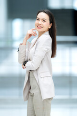 Successful Asian woman leader in beige suit smiling indoors, representing ambition, empowerment,...