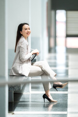 Relaxed female executive in beige suit smiling while sitting indoors, representing confidence,...