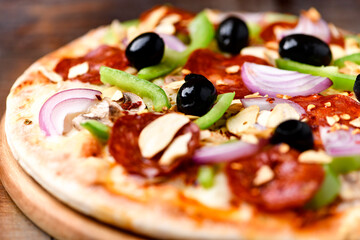 Pizza with chorizo ​​sausage, mozzarella cheese, green pepper and black olives. Rustic wooden background. Soft focus.	