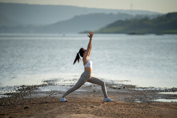 Sporty Asian woman in activewear doing side stretch exercise outdoors by the water, symbolizing...