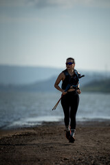 Female trail runner exercising with trekking poles by the lake, showing strength, motivation, and active lifestyle.