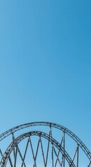 Striking steel roller coaster tracks curve against a vibrant blue sky.