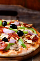 Pizza with chorizo ​​sausage, mozzarella cheese, green pepper and black olives. Rustic wooden background. Soft focus.	