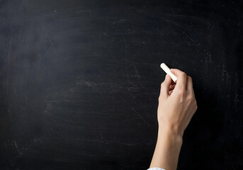 Naklejka premium A hand writes on a blackboard with a white chalk.