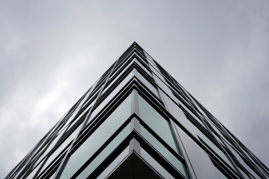 Modern glass building corner captured from low angle, emphasizing sharp lines, minimalism, and urban architectural design against cloudy sky.