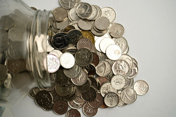 Glass jar tipped over with scattered coins spilling out, symbolizing savings, financial planning, money storage, and the concept of wealth accumulation.
