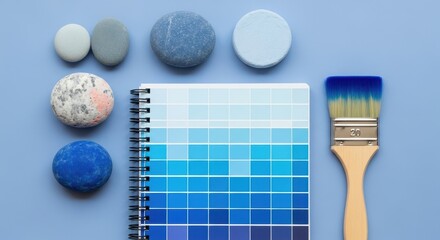 Top view of blue paint swatches and stones arranged with a paintbrush on a blue background