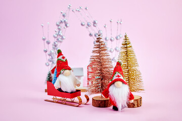 Christmas image on which one gnome is riding on a sled, and the second is hiding behind Christmas trees, winter fun on a pink background, horizontally