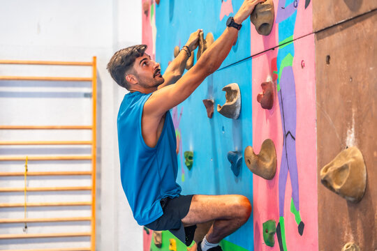 Determined male athlete climbing challenging indoor rock wall