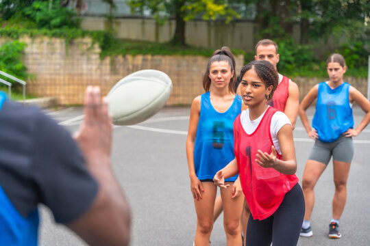 Coach throwing rugby ball to female players during training