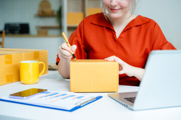Closeup of young Caucasian woman preparing cardboard box for shipping in a home office. E-commerce,...