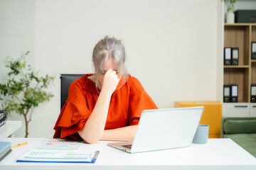 Overwhelmed young woman stressed at her desk with a laptop and reports in a modern office. Concept of burnout, workplace pressure