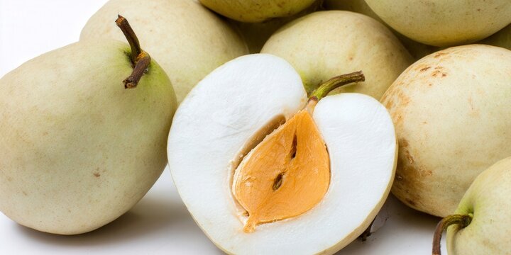 Fresh star apples, one cut open showing the vibrant orange and white pulp.