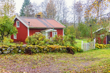 Red idyllic wooden croft with a stone wall and a gate to the garden © Lars Johansson