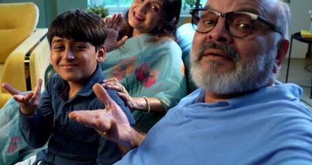 Indian grandparents with grandchild attending video call using smartphone while sitting on sofa in modern home indoors, happy family bonding together, smiling senior couple with kid enjoying selfie - Powered by Adobe