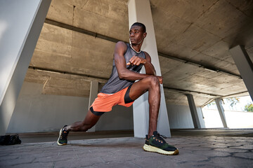 Athletic man stretching under a concrete overpass during a training session