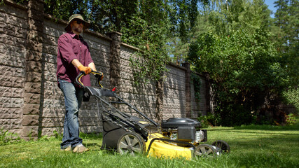 Man mowing lawn with a yellow electric mower in a sunny backyard