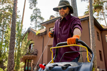 Man mowing lawn near family home surrounded by lush green trees