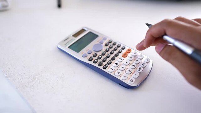 Close-up of hands using a scientific calculator on a white surface