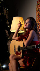 Beautiful woman with guitar in hands and glass of champagne celebrates christmas at home
