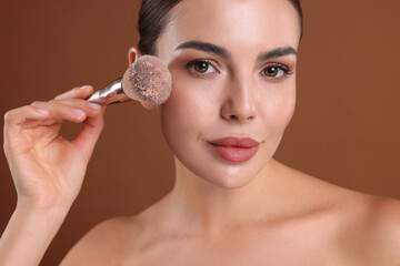 Beautiful woman applying makeup with brush on brown background