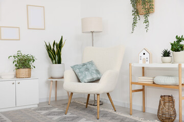 Stylish armchair, lamp, cabinet, console table and houseplants in room. Interior design