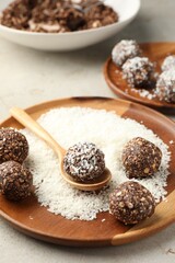 Making tasty chocolate candies with nuts and coconut flakes at light table, closeup
