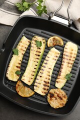 Delicious grilled courgette slices with garlic, lemon and parsley in pan on grey textured table, flat lay