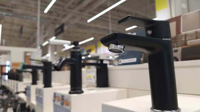 Modern black faucets displayed in hardware store aisle with bright lighting