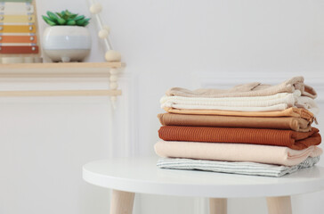 Stack of clean baby clothes on white table indoors, space for text