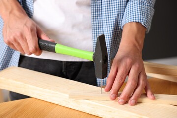 Man hammering nail into wooden plank indoors, closeup
