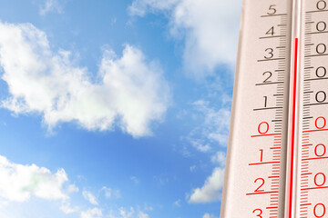 High temperature on thermometer against blue sky on sunny day. Summer weather