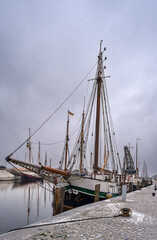 Obraz premium Ein wolkenverhangener Winterhimmel spannt sich über den Greifswalder Museumshafen, an dem mehrere Rad- und Wanderwege vorbeilaufen – Inschriften retuschiert
