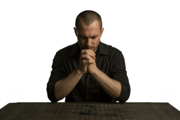 Man in his late 30s with a shaved head praying earnestly in a somber setting transparent background
