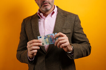 Close-up of a man in a brown blazer and pink shirt holding a 20 euro banknote