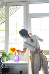Woman in rubber gloves and apron manually washes window balcony of house with rag cleaner and mop inside interior. Restoring order and cleanliness in spring, cleaning servise