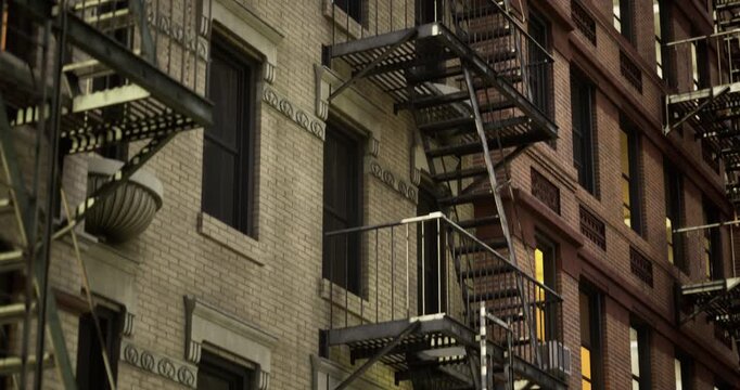 Steel fire escapes climb the sides of aged brick buildings in a bustling city. Windows glow warmly, highlighting the charm of urban life. The scene captures a tranquil twilight moment.