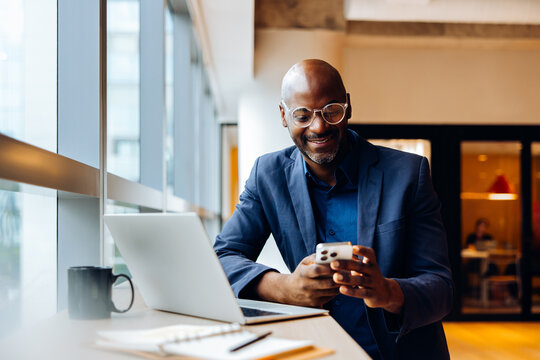 Man in an office wearing glasses working with phone and laptop