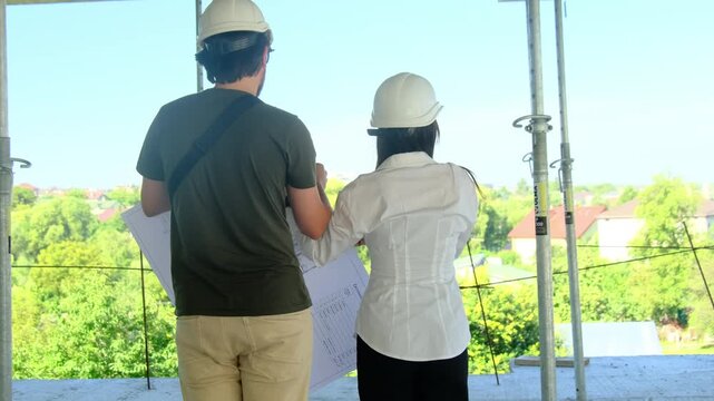 Male and female engineers walk around unfinished building. Specialists study special layout of building and discuss scope of work process